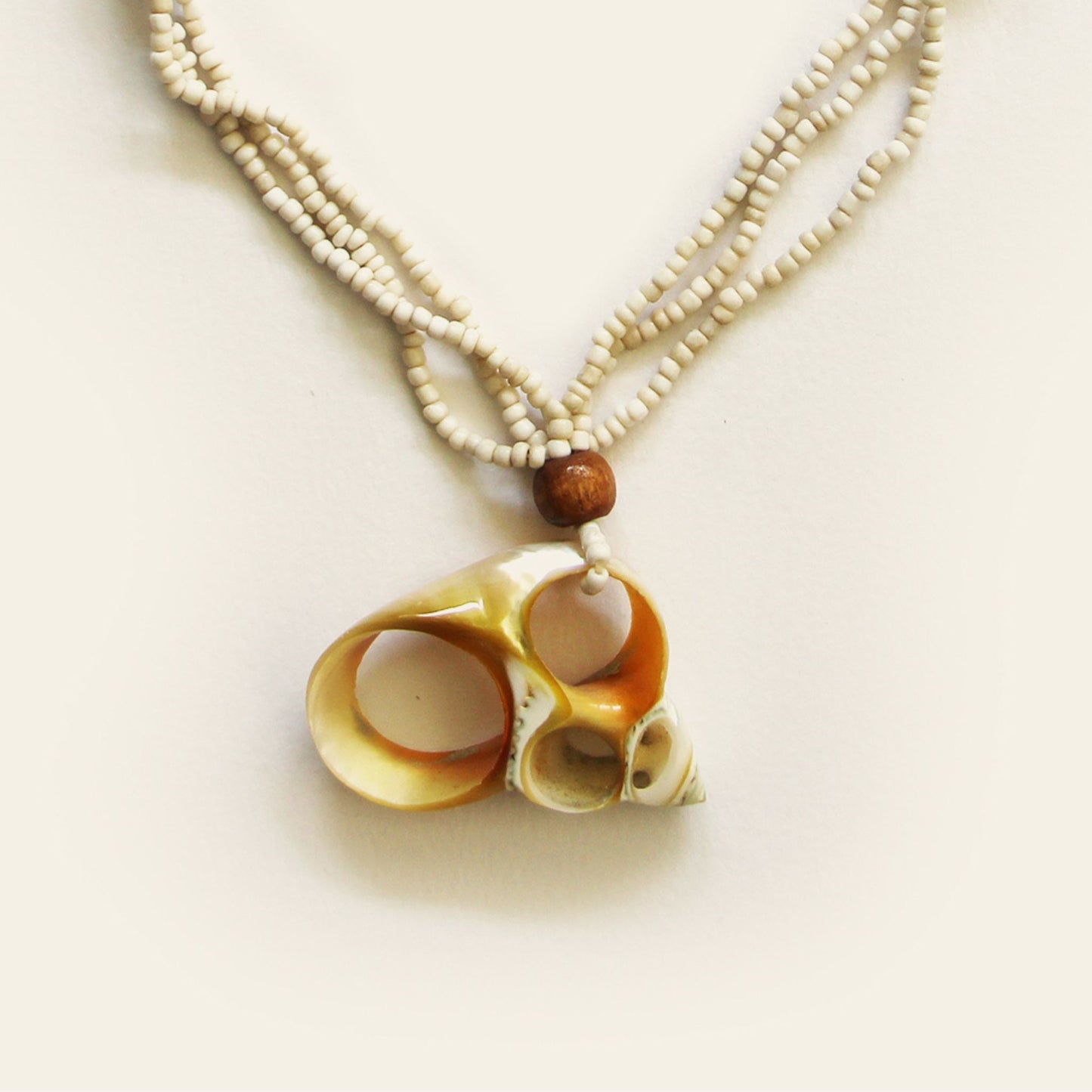 Closeup of handmade necklace with sand seed beads, wooden accents, and a natural oval shell pendant with mini shell charms — by Nayabijou.