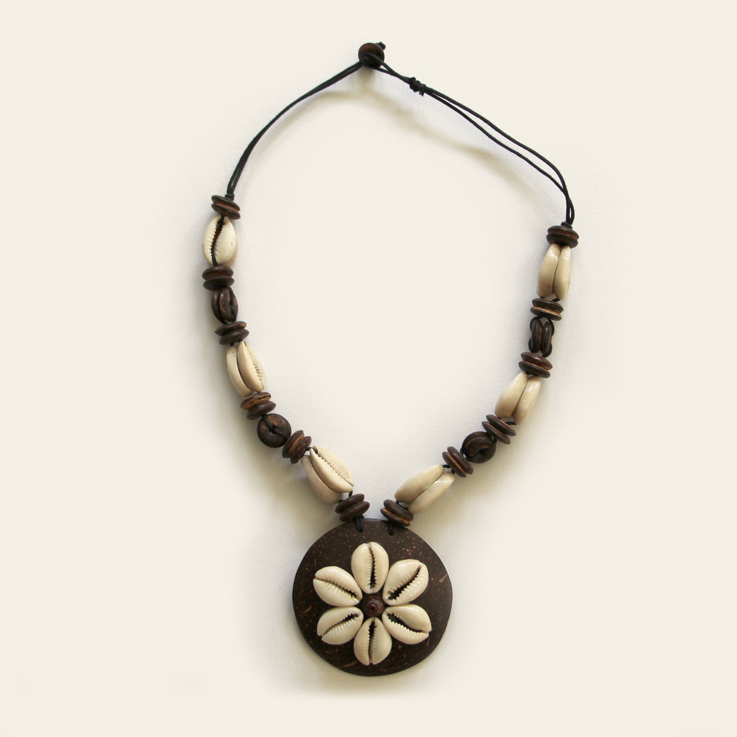 Handmade necklace with natural cowrie shells arranged on a dark round pendant, paired with wood and shell beads on a black cord — by Nayabijou.