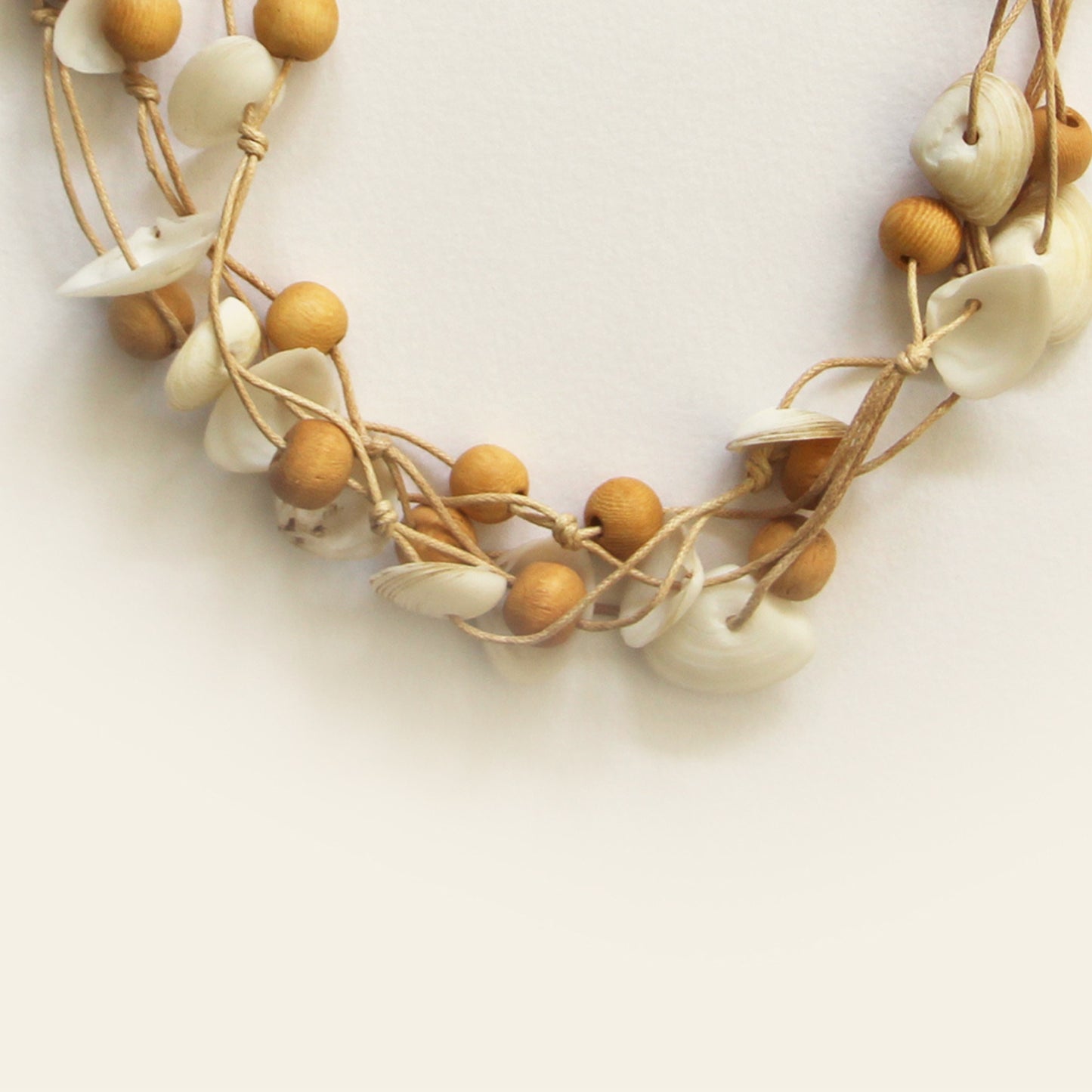 Closeup of handmade sand-toned necklace with natural white shell chips and light wooden beads on layered threads — Nayabijou.