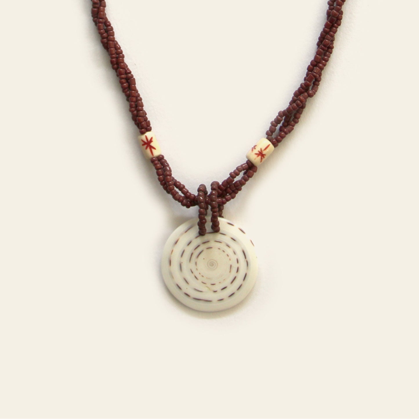 Handmade necklace with brown seed beads, dark wooden accents, and a round spiral-patterned shell pendant — by Nayabijou.