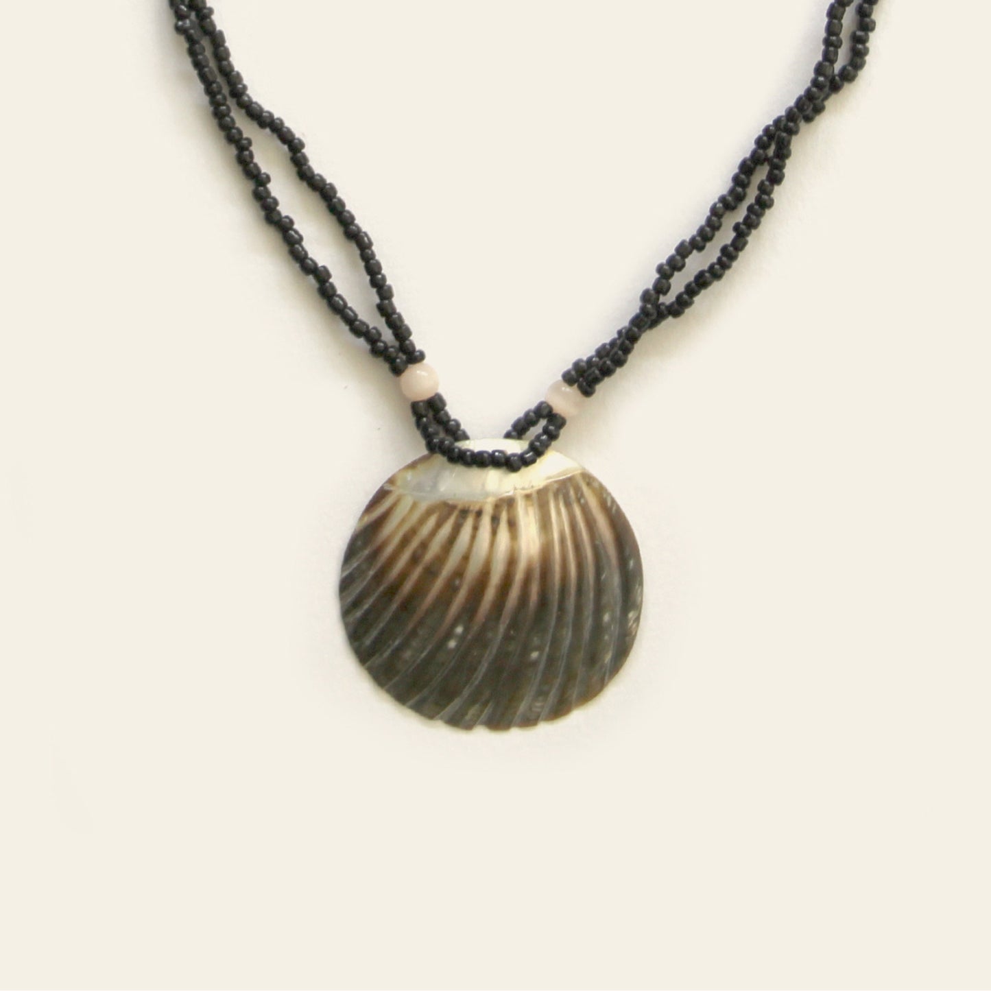 Closeup of handmade necklace with black seed beads and a dark scallop shell pendant – Nayabijou.
