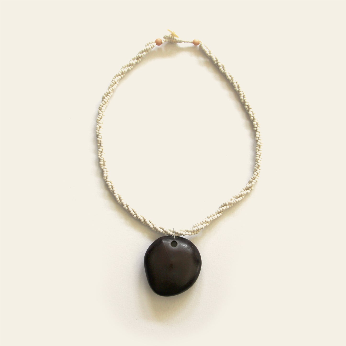 Handmade necklace with off-white seed beads and a smooth black wooden pendant, designed by Nayabijou.