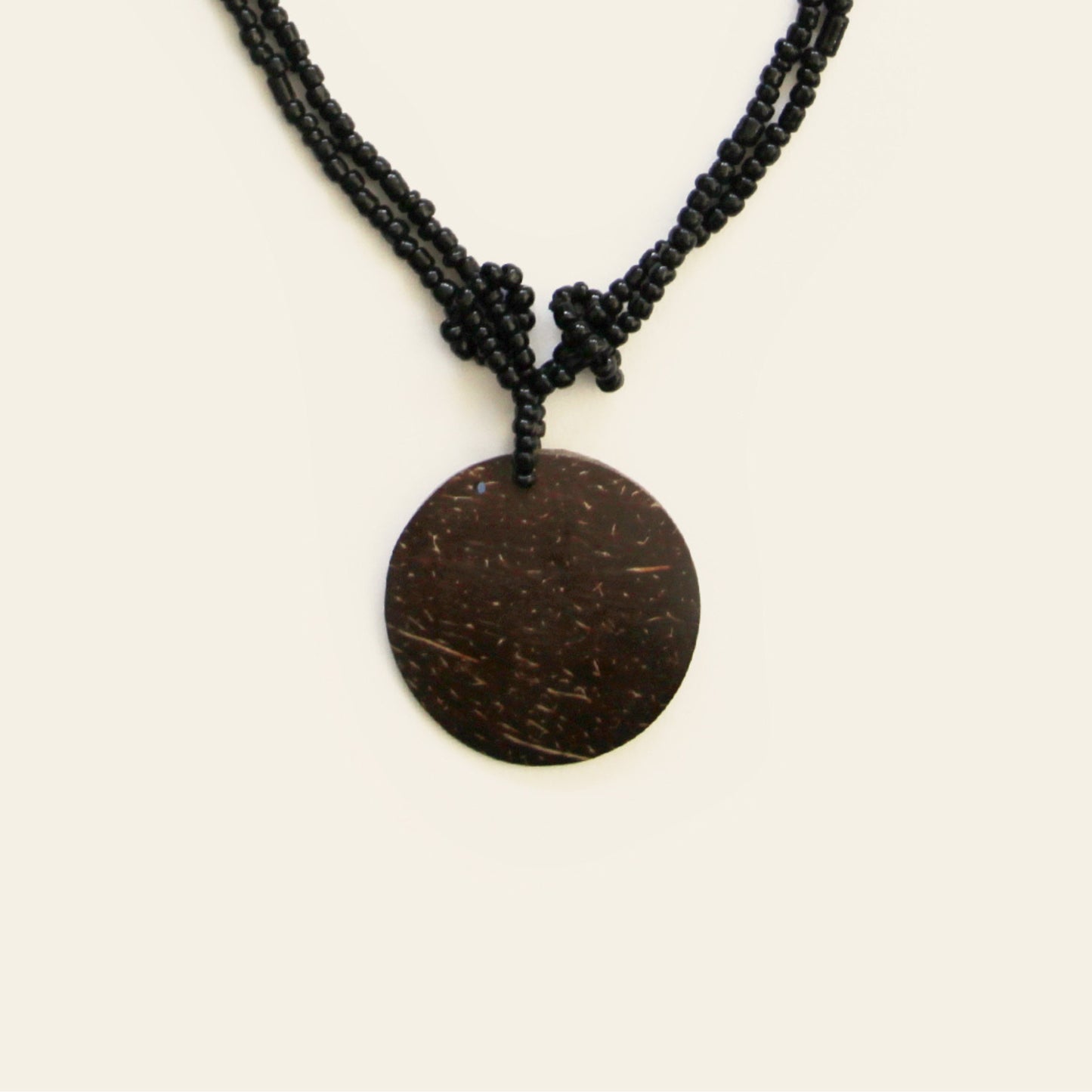 Close-up of coconut pendant with knotted black seed bead strands