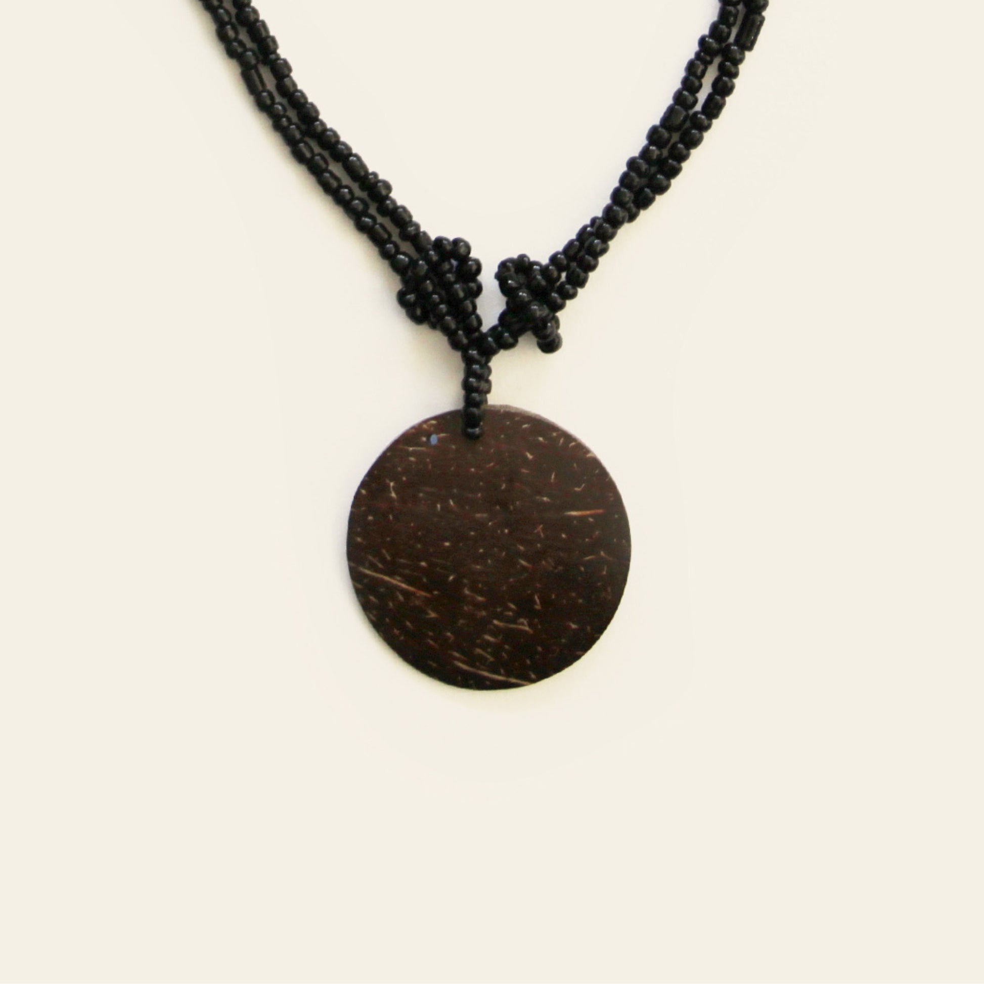 Close-up of coconut pendant with knotted black seed bead strands