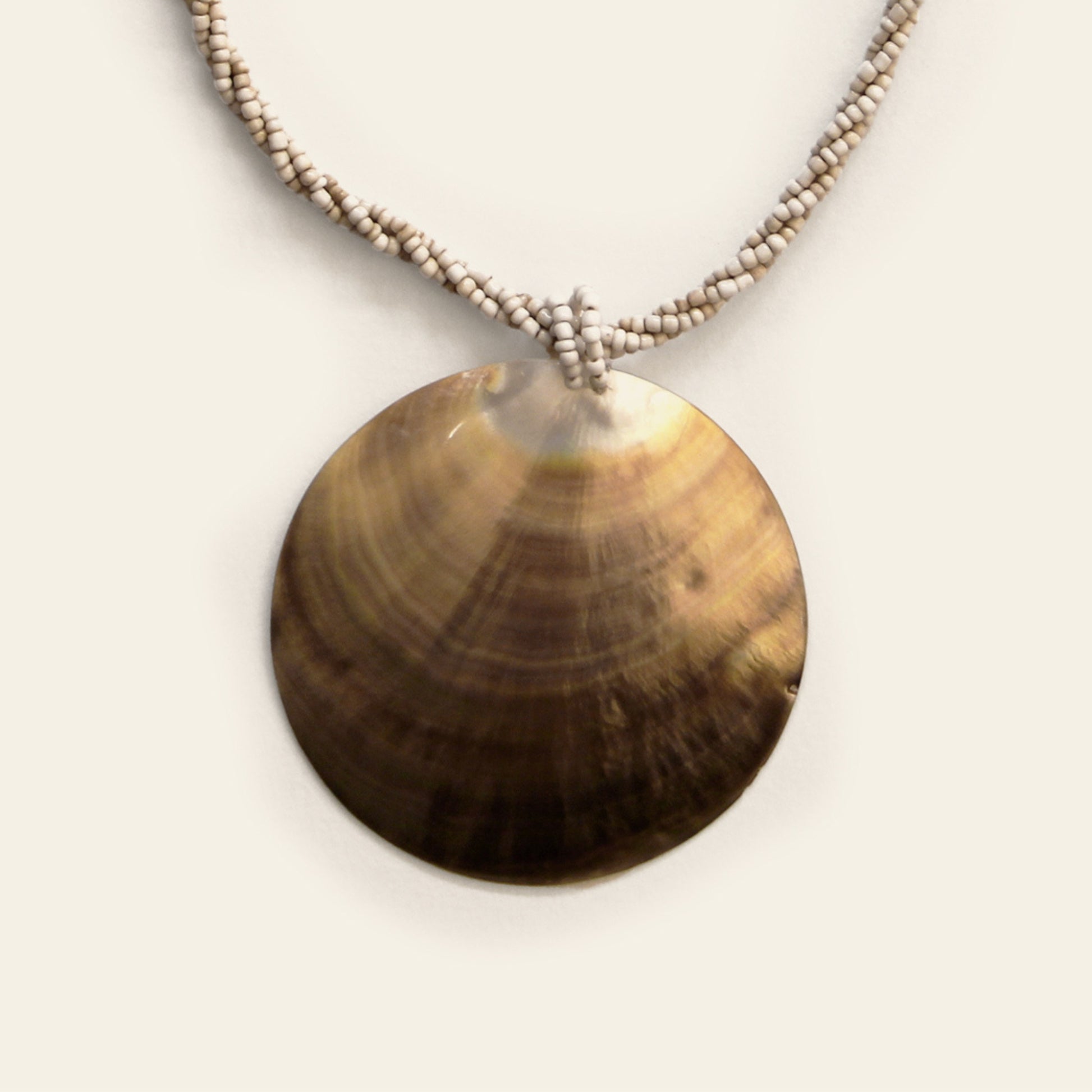 Closeup of handmade round bronze-toned shell necklace with beige seed beads – Nayabijou.