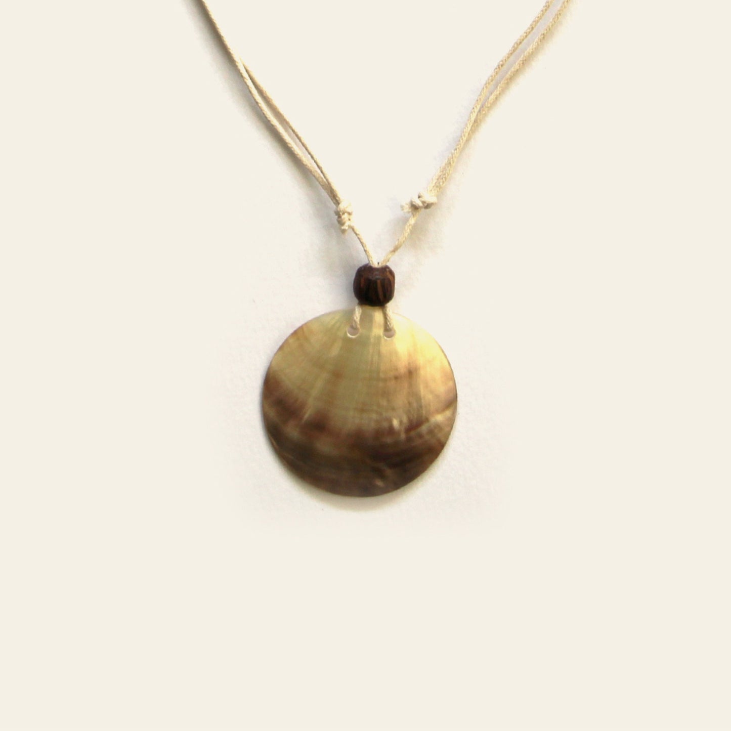 Closeup of handmade necklace with beige cord and round natural Mother of Pearl pendant – Nayabijou.