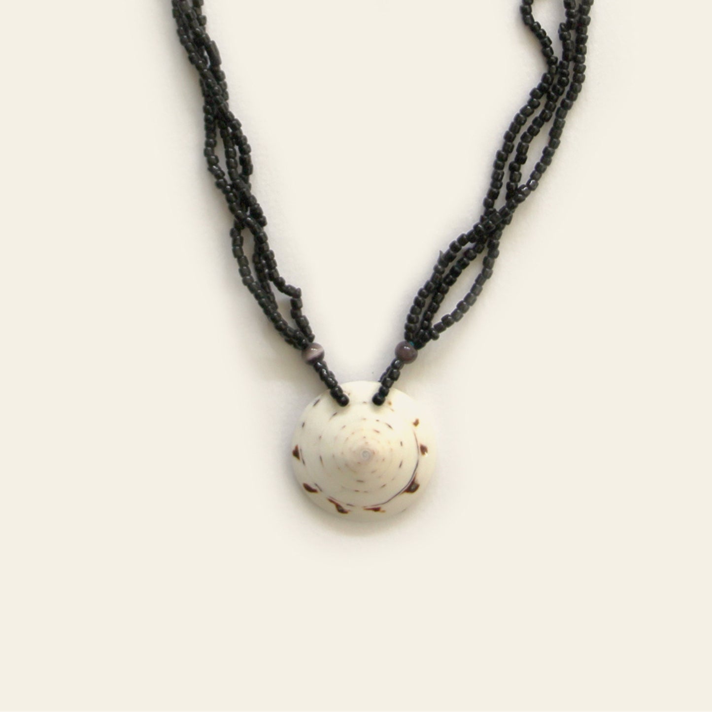 Closeup of handmade necklace with layered black seed beads and a white natural shell pendant — Nayabijou.