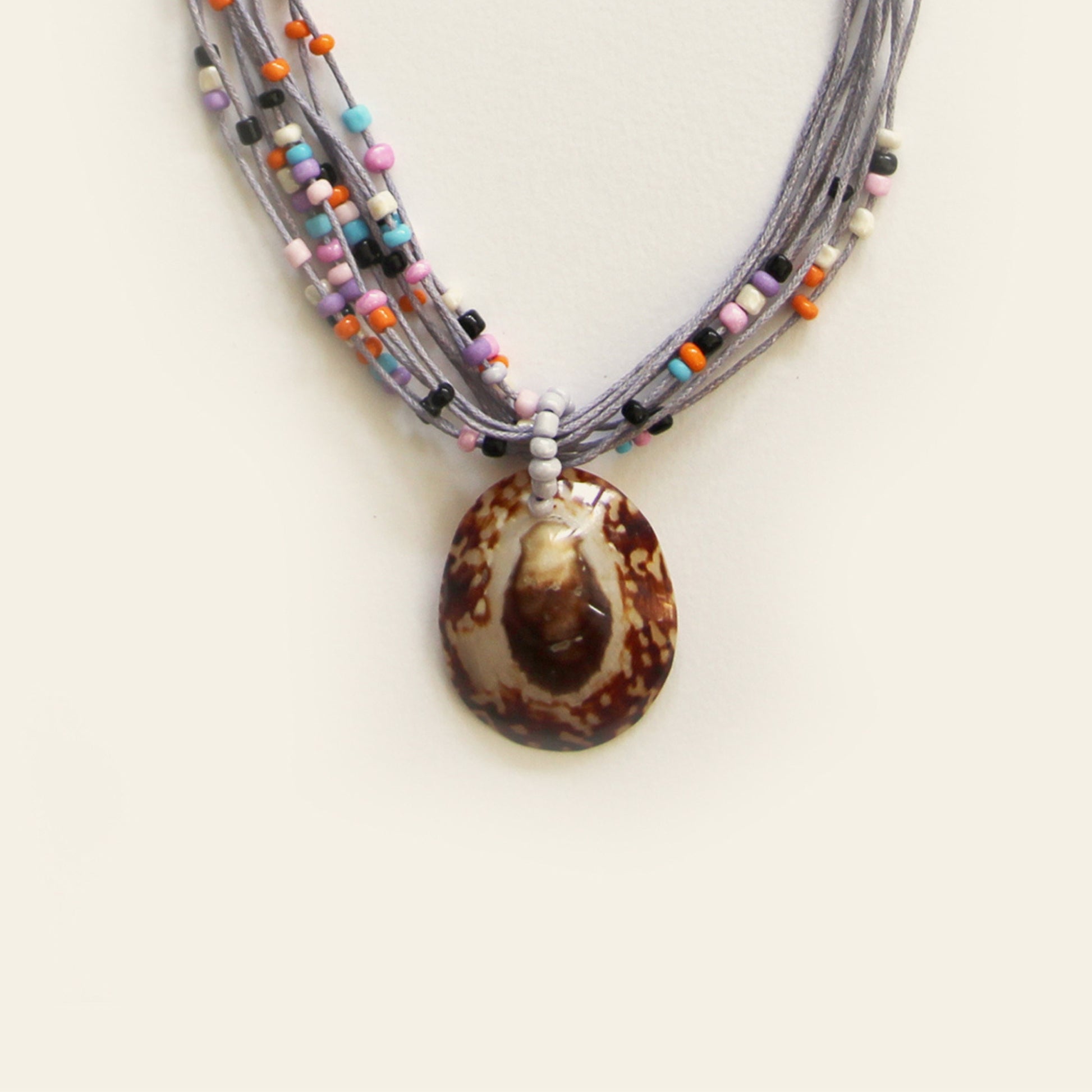 Closeup of handmade necklace with gray threads, multicolor beads, and a brown shell pendant — crafted by Nayabijou.
