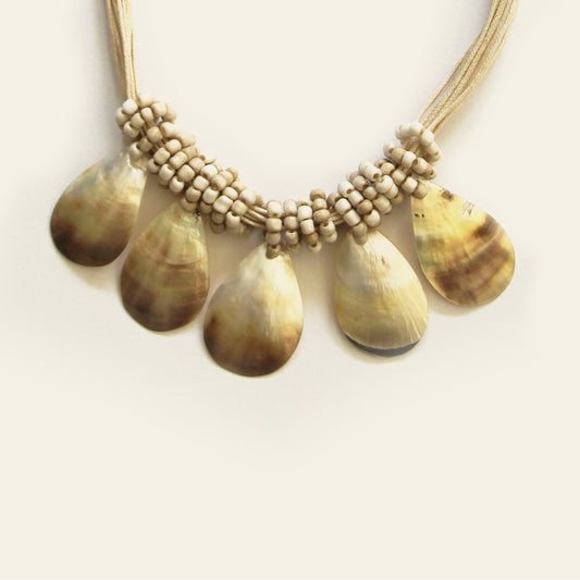 Closeup of natural sand-colored teardrop shell necklace with layered black cord and artisanal accents- Nayabijou