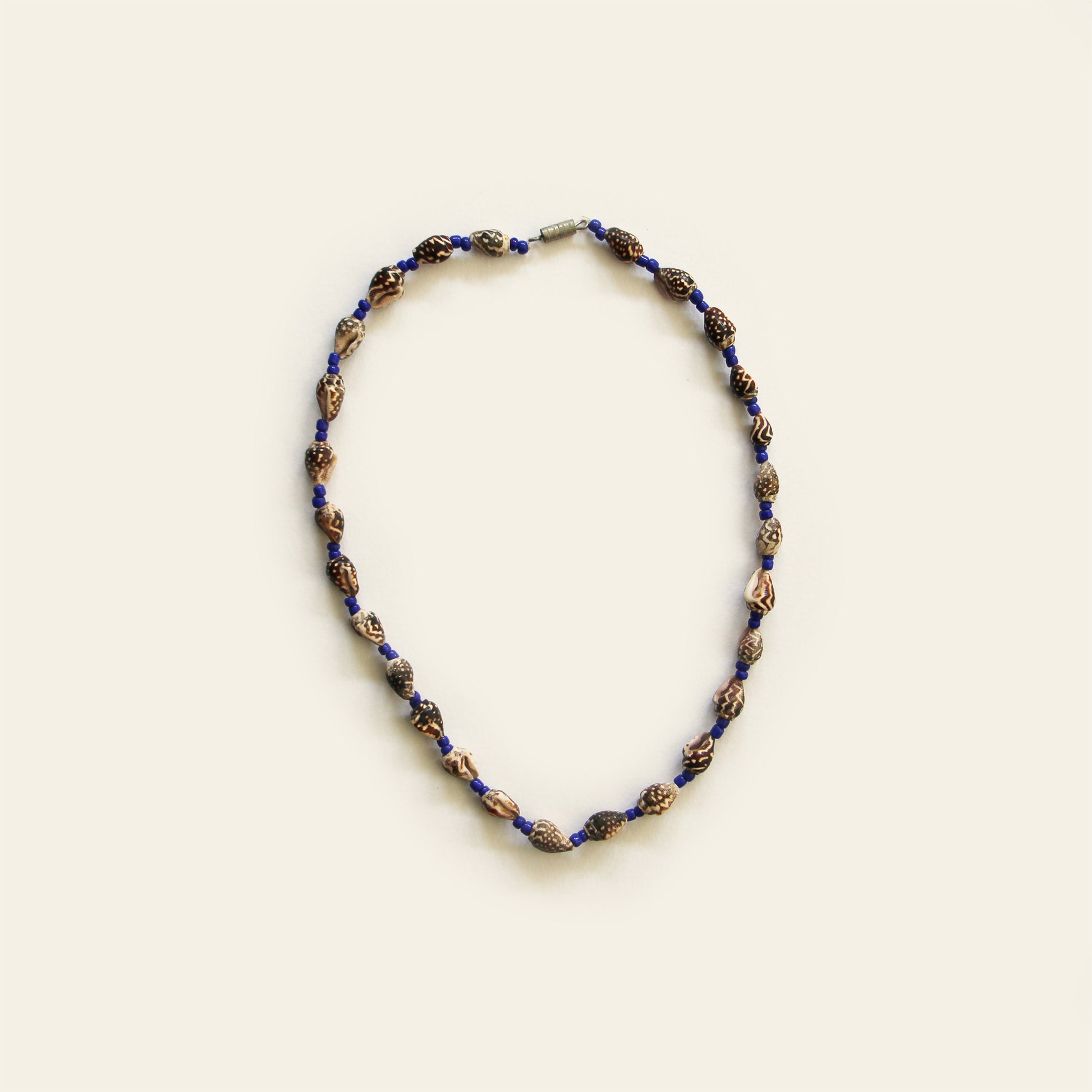 Handmade necklace with carved brown beads, small shell accents, and deep blue seed beads — by Nayabijou.