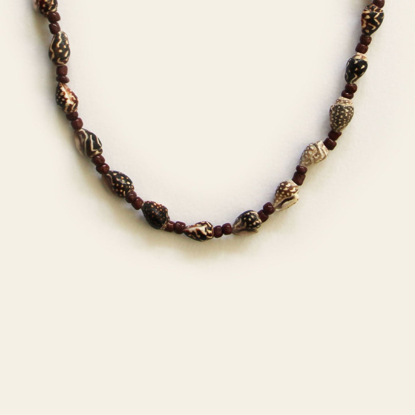 Closeup of handmade necklace with carved brown beads, small shell accents, and warm brown seed beads — by Nayabijou.