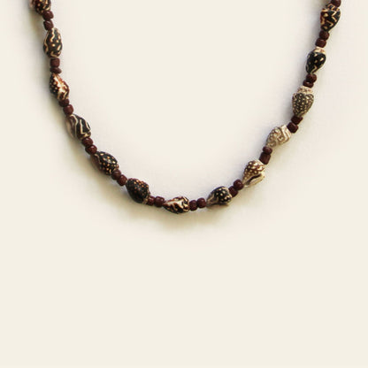 Closeup of handmade necklace with carved brown beads, small shell accents, and warm brown seed beads — by Nayabijou.