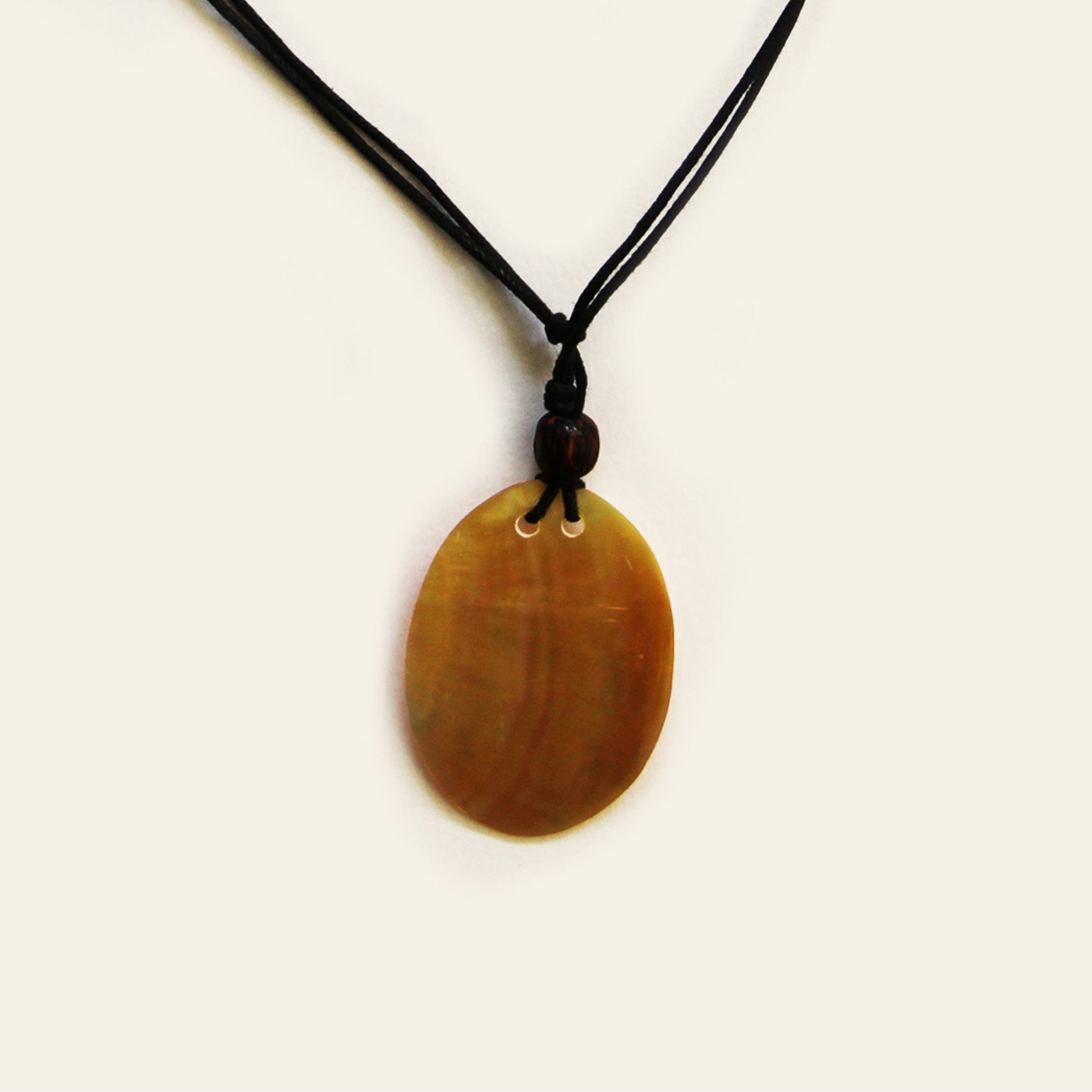 Closeup of a smooth shell pendant in warm honey tones, strung on a simple black cord. Clean, lightweight, and easy to wear — this one adds a natural touch to everyday outfits.