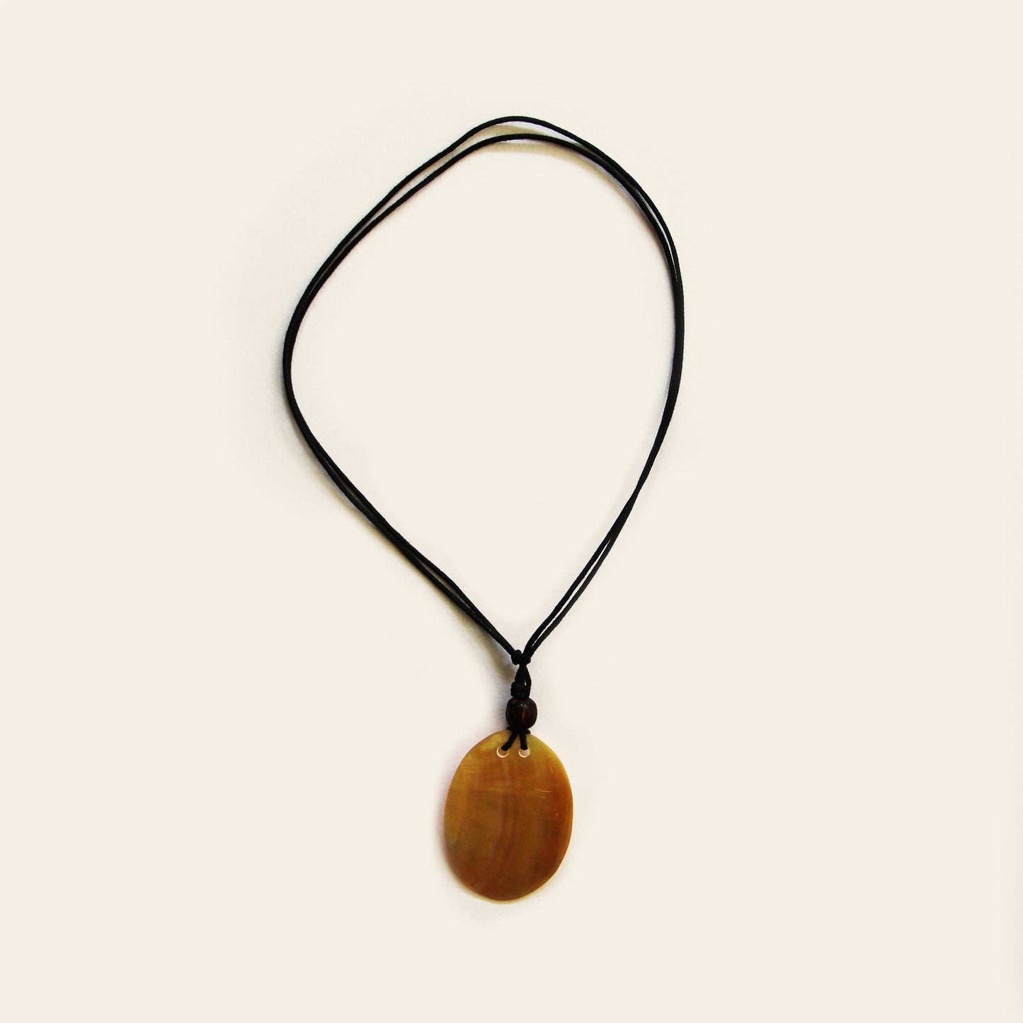 A smooth shell pendant in warm honey tones, strung on a simple black cord. Clean, lightweight, and easy to wear — this one adds a natural touch to everyday outfits.