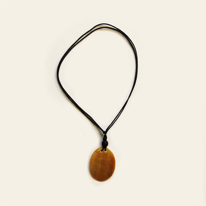 A smooth shell pendant in warm honey tones, strung on a simple black cord. Clean, lightweight, and easy to wear — this one adds a natural touch to everyday outfits.