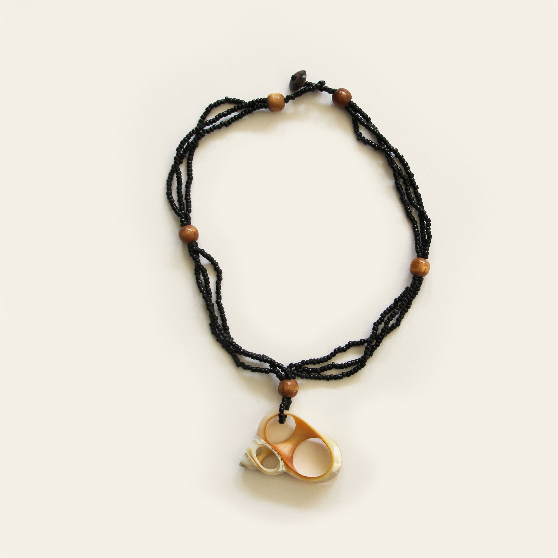 Handmade necklace with black seed beads, wooden accents, and a natural oval shell pendant with mini shell charms — by Nayabijou.