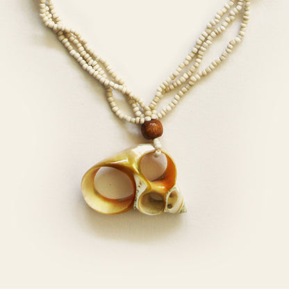 Closeup of handmade necklace with sand seed beads, wooden accents, and a natural oval shell pendant with mini shell charms — by Nayabijou.