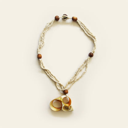 Handmade necklace with sand seed beads, wooden accents, and a natural oval shell pendant with mini shell charms — by Nayabijou.
