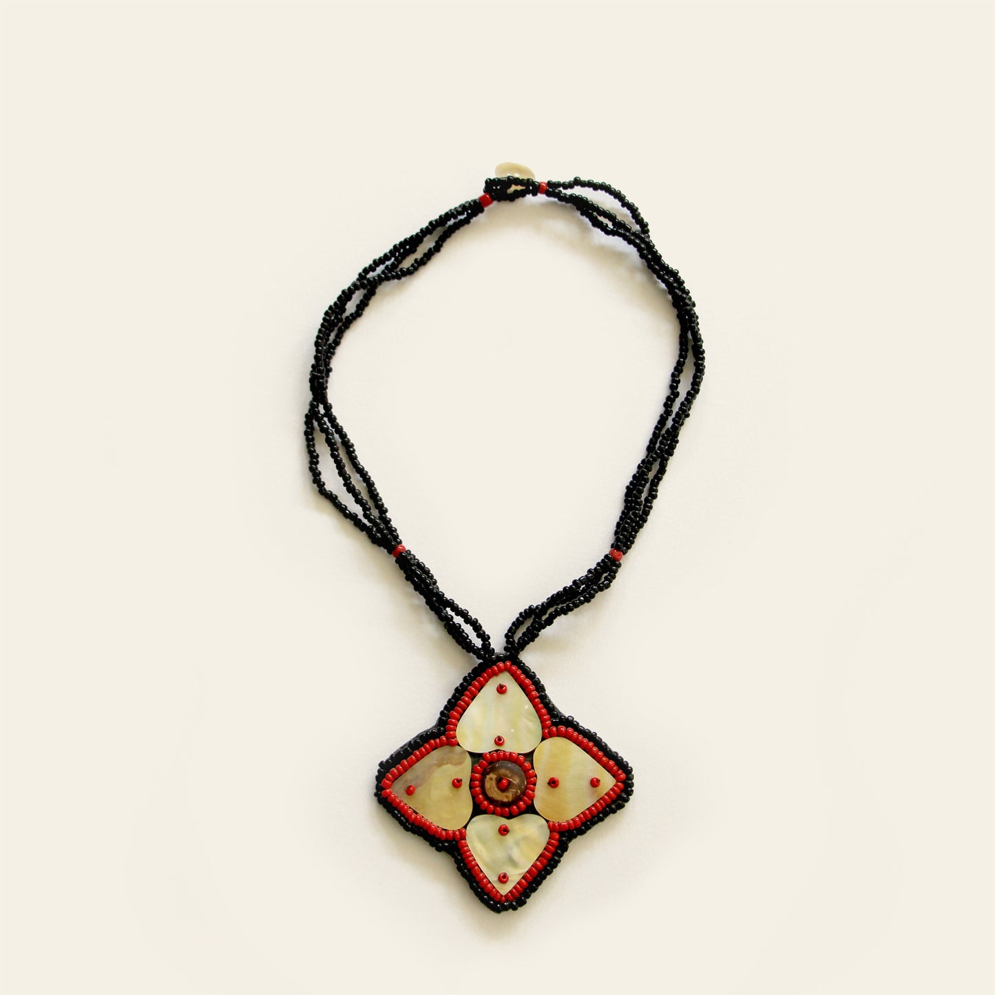 Handmade necklace featuring a mother-of-pearl flower pendant with red bead detailing, strung on triple black seed bead strands — by Nayabijou.