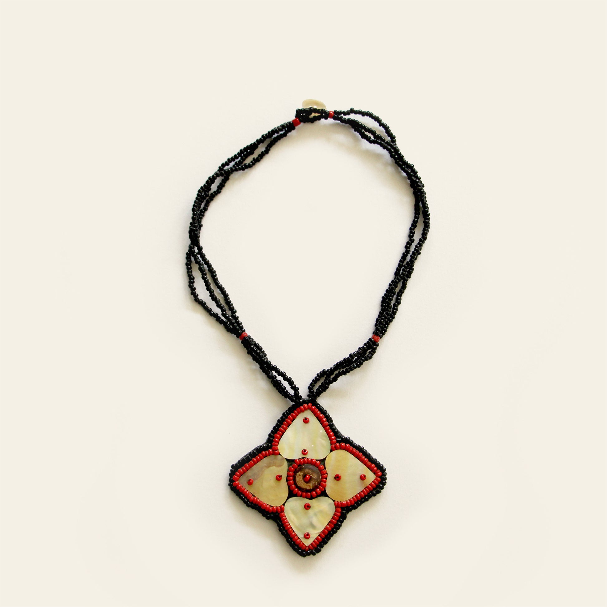 Handmade necklace featuring a mother-of-pearl flower pendant with red bead detailing, strung on triple black seed bead strands — by Nayabijou.