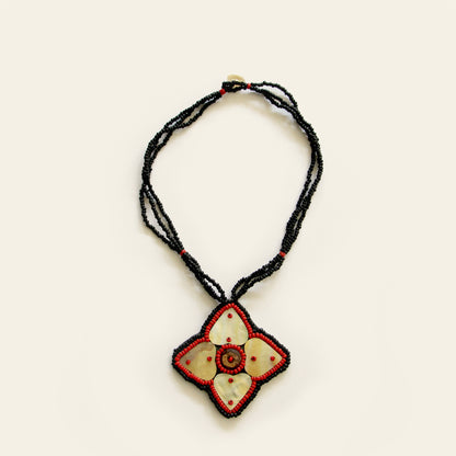 Handmade necklace featuring a mother-of-pearl flower pendant with red bead detailing, strung on triple black seed bead strands — by Nayabijou.