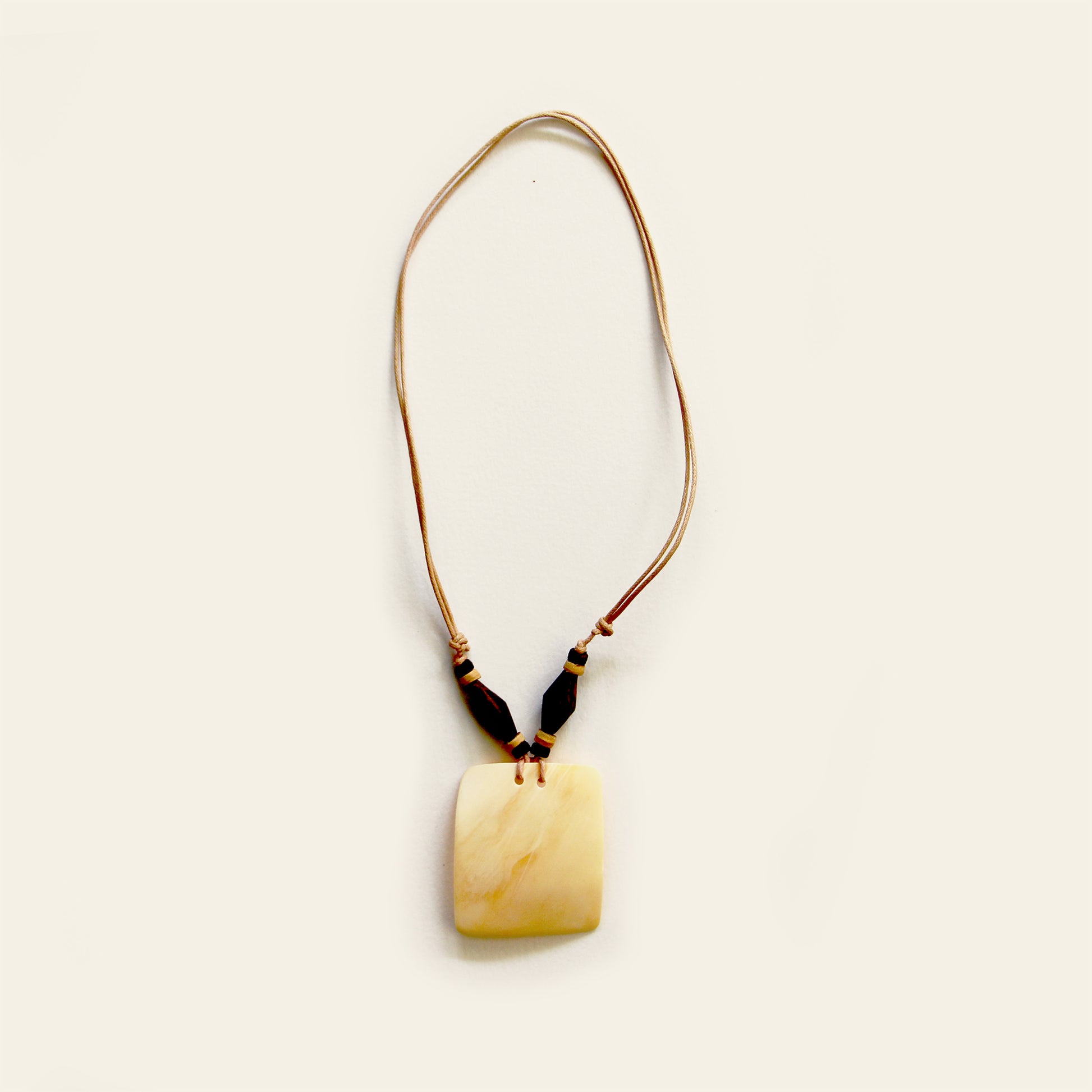 Handmade necklace with a tan leather cord, dark wood beads, and a square-shaped beige shell pendant — by Nayabijou.