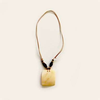 Handmade necklace with a tan leather cord, dark wood beads, and a square-shaped beige shell pendant — by Nayabijou.