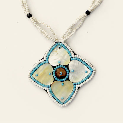 Closeup of handmade white beaded necklace featuring a large mother-of-pearl flower pendant with blue accents and central shell detail – Nayabijou.