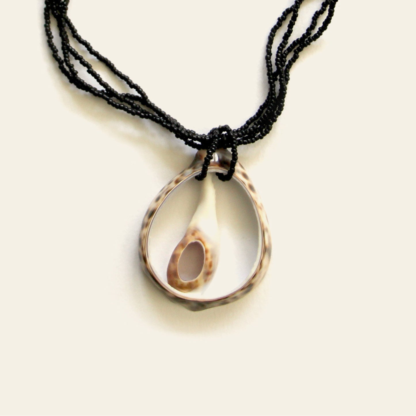 Closeup of handmade necklace with a duo of open shell pendants on black seed bead strands — Nayabijou.