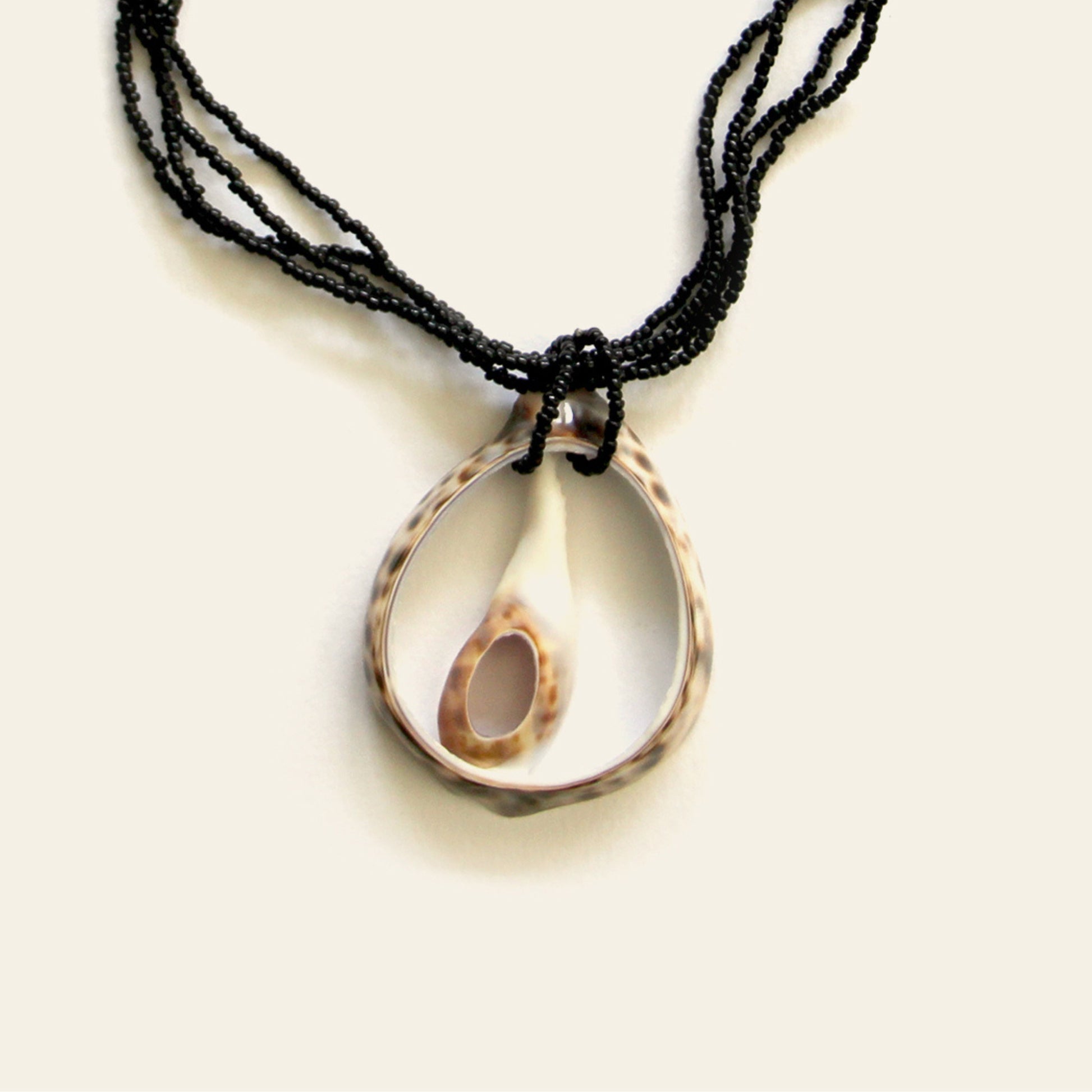 Closeup of handmade necklace with a duo of open shell pendants on black seed bead strands — Nayabijou.