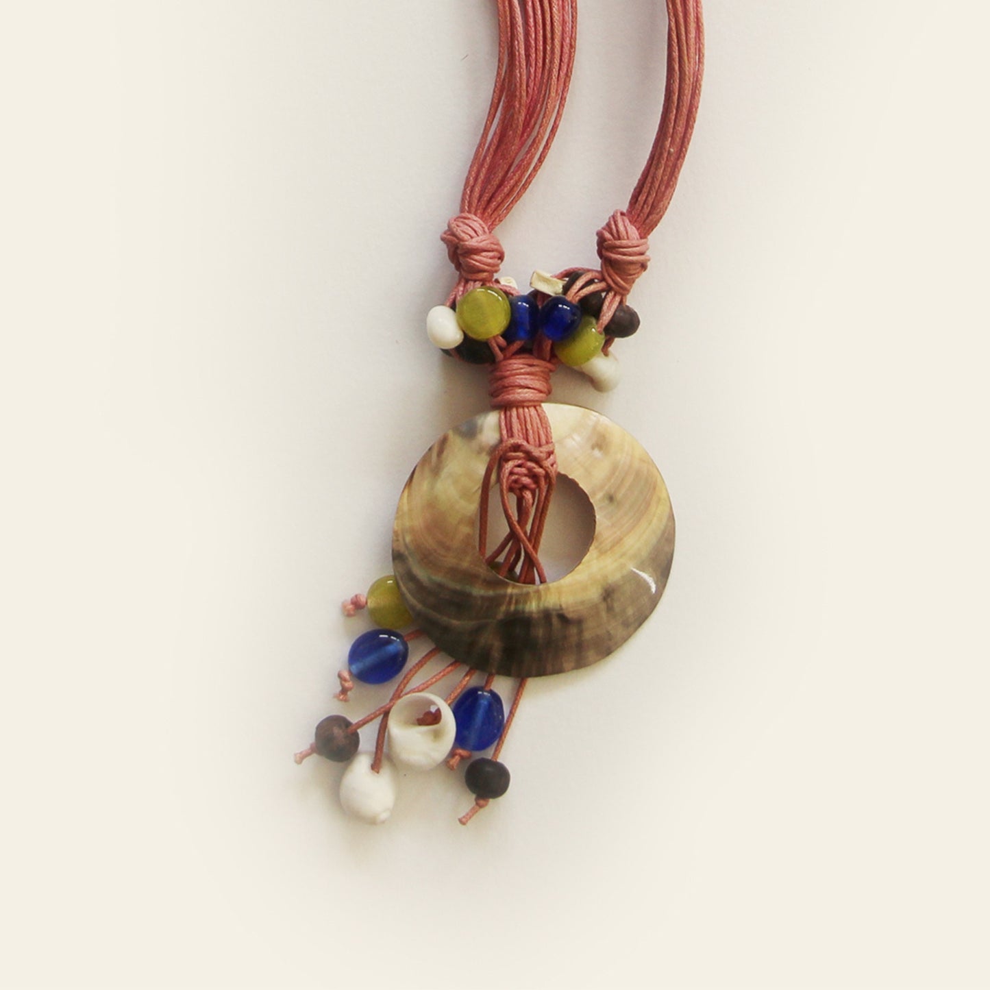 Closeup of a handmade necklace with mauve cords, a round shell pendant, and colorful natural beads – by Nayabijou.