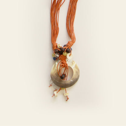 Closeup of a handmade necklace with burnt orange cords, a shell pendant, and small natural beads – by Nayabijou.