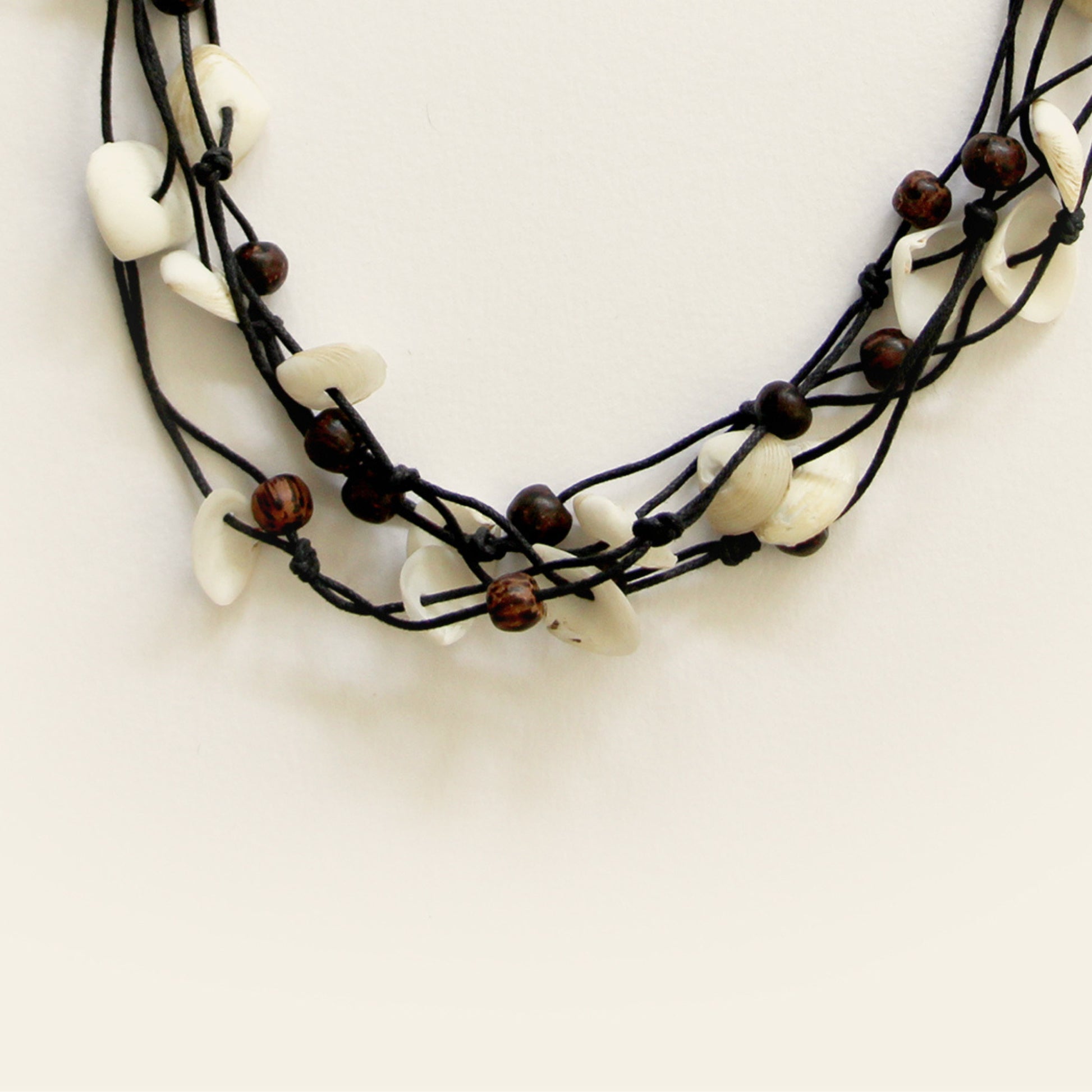 Closeup of handmade black cotton thread necklace with layered white shell pieces and dark wooden beads — Nayabijou.
