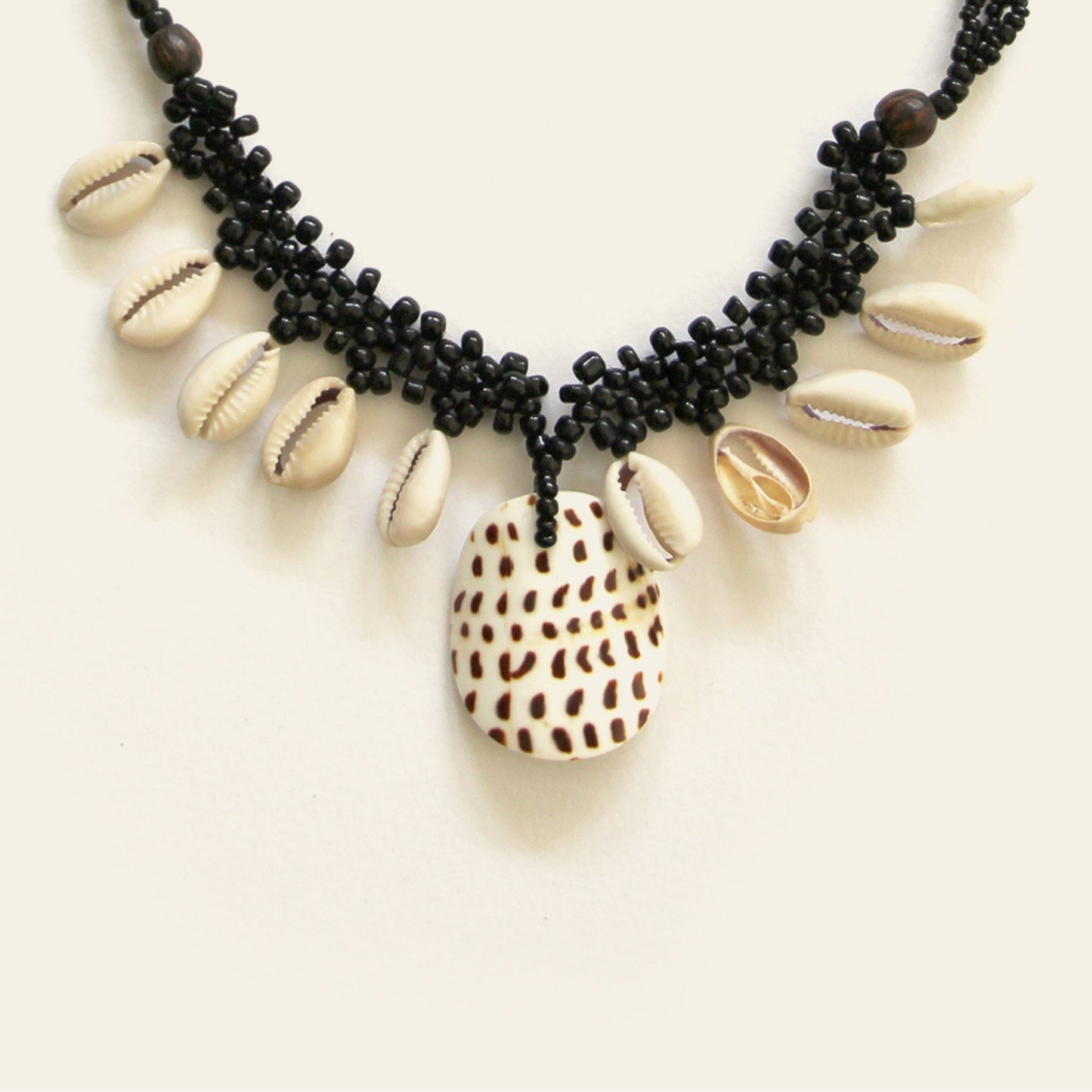 Closeup of handmade black beaded necklace with dangling shells and a central spotted shell pendant – Nayabijou.