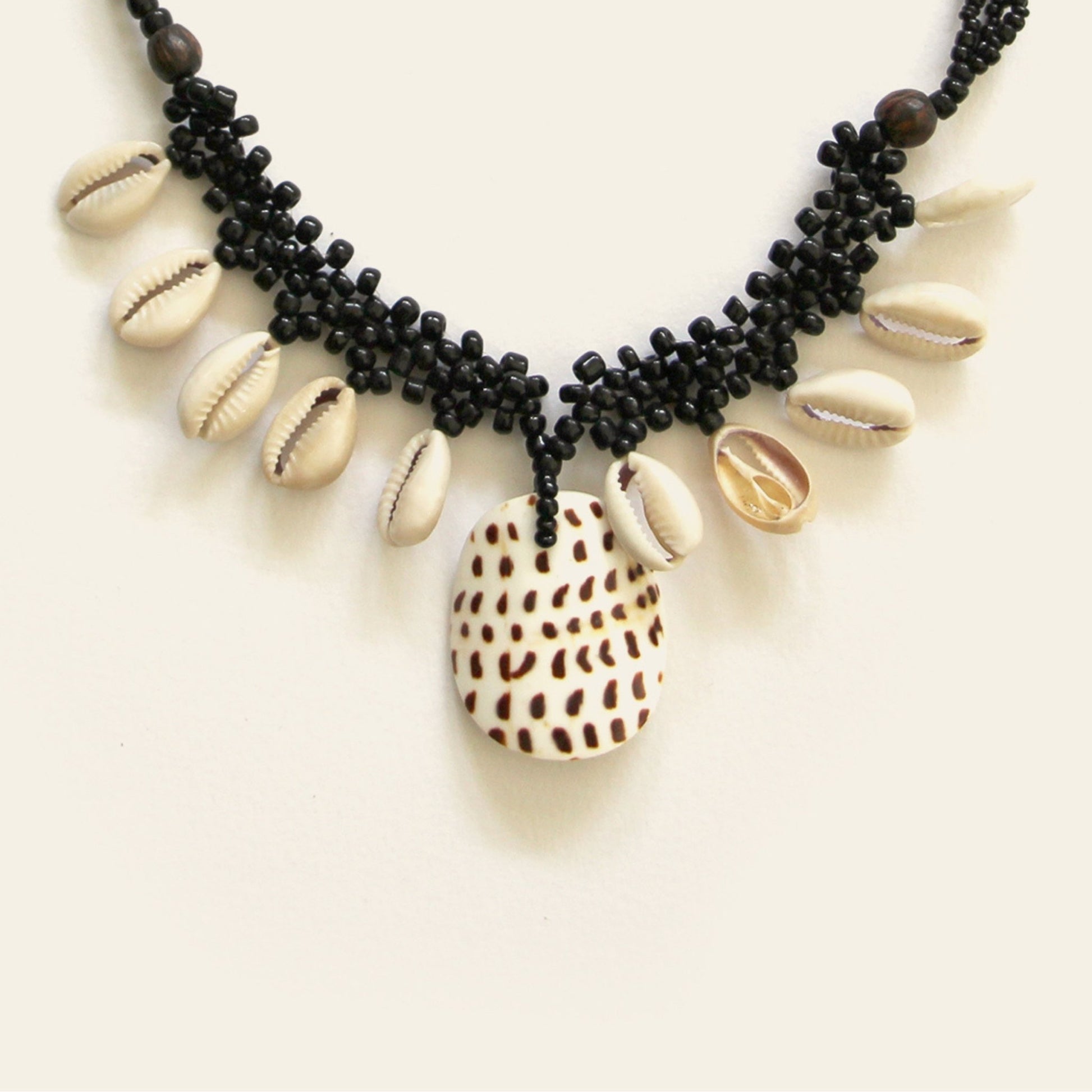 Closeup of handmade black beaded necklace with dangling shells and a central spotted shell pendant – Nayabijou.