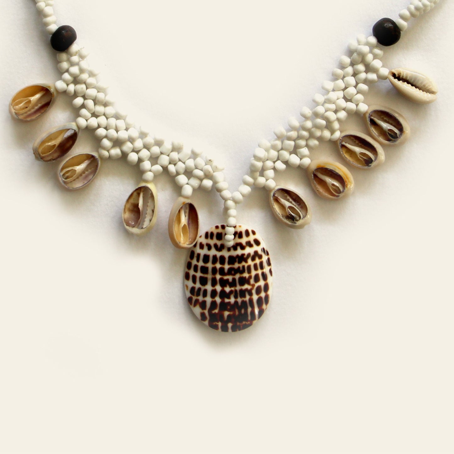 Closeup of handmade black beaded necklace with dangling shells and a central spotted shell pendant – Nayabijou.