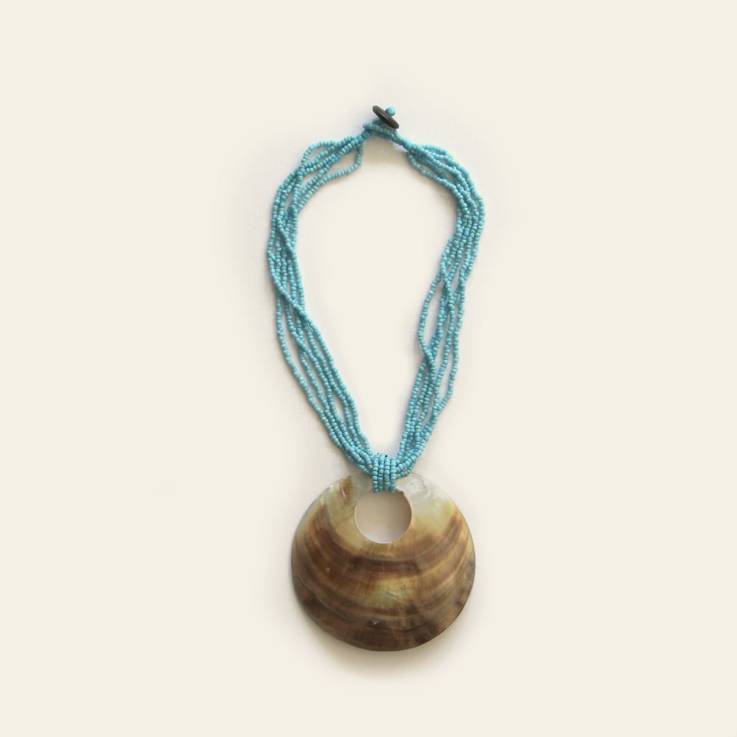 Handmade necklace with a large round shell pendant and layered turquoise seed bead strands — by Nayabijou.