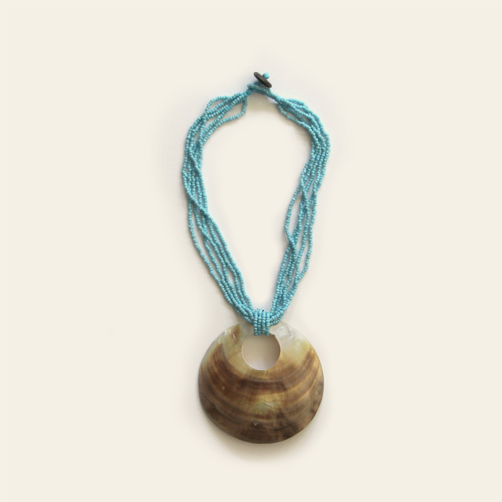 Handmade necklace with a large round shell pendant and layered turquoise seed bead strands — by Nayabijou.