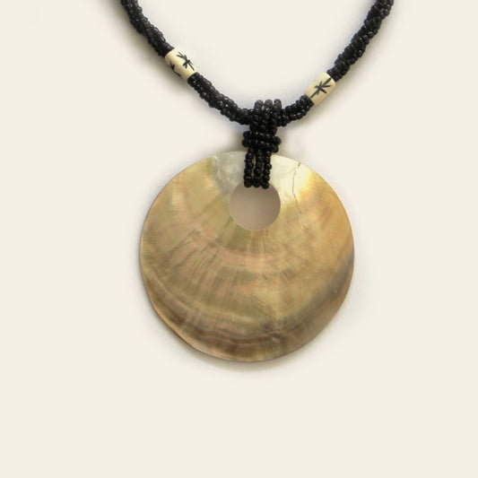 Closeup of handmade necklace with black seed beads, ivory accents, and a large golden-brown round shell pendant — by Nayabijou.