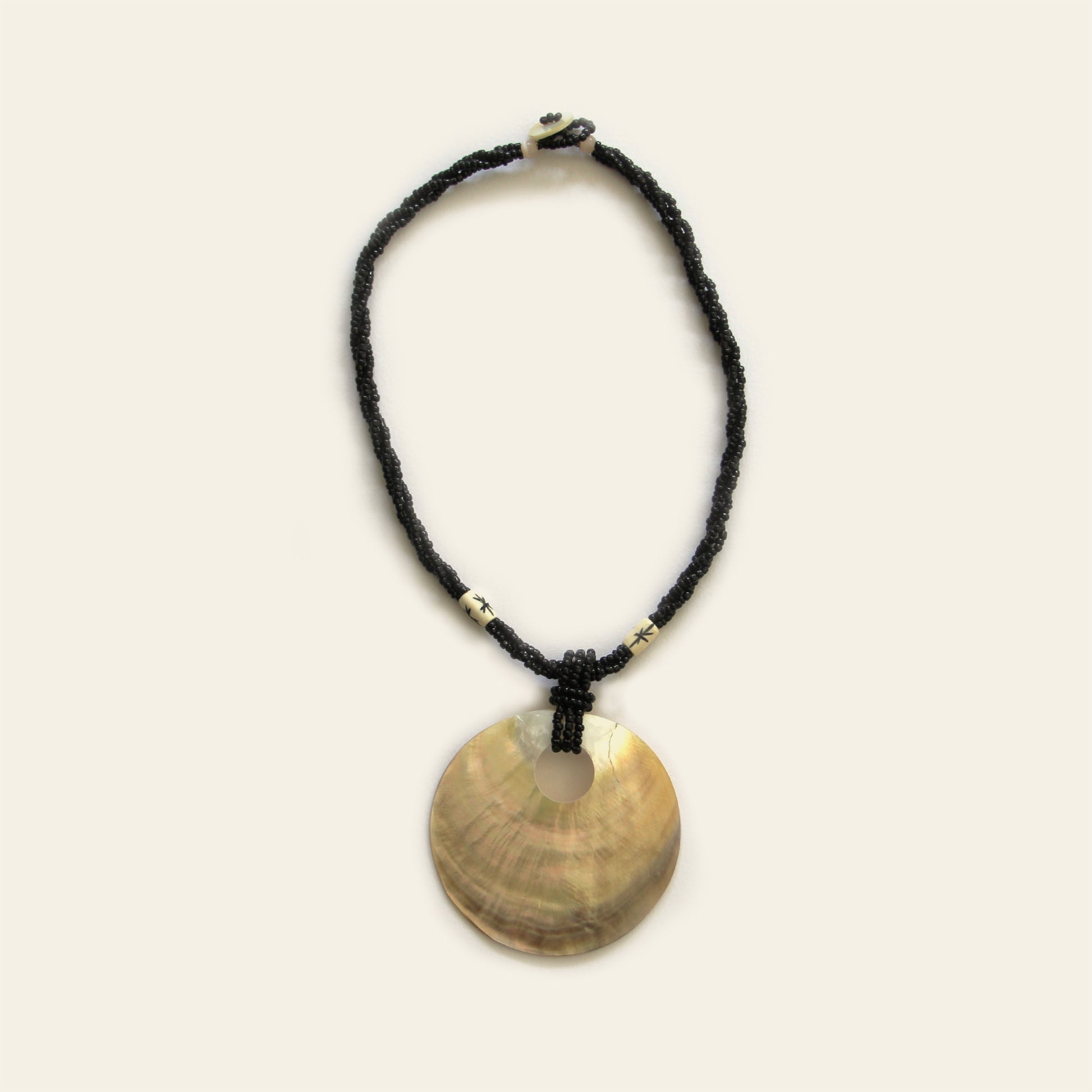 Handmade necklace with black seed beads, ivory accents, and a large golden-brown round shell pendant — by Nayabijou.
