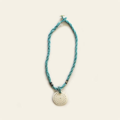 Handmade necklace with Turquoise seed beads, dark wooden accents, and a round spiral-patterned shell pendant — by Nayabijou.