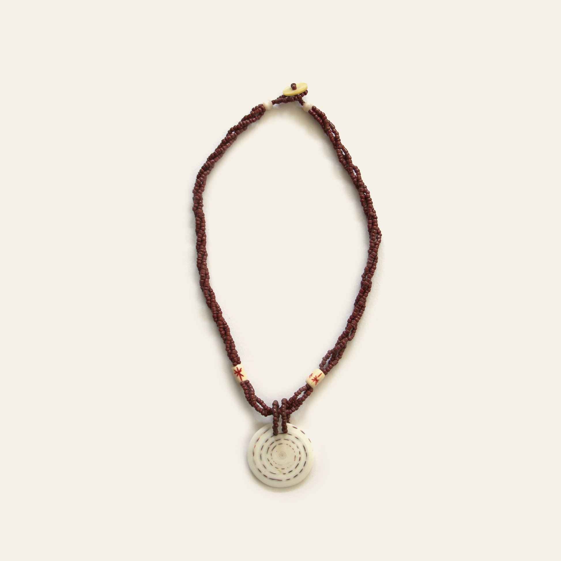 Handmade necklace with brown seed beads, dark wooden accents, and a round spiral-patterned shell pendant — by Nayabijou.
