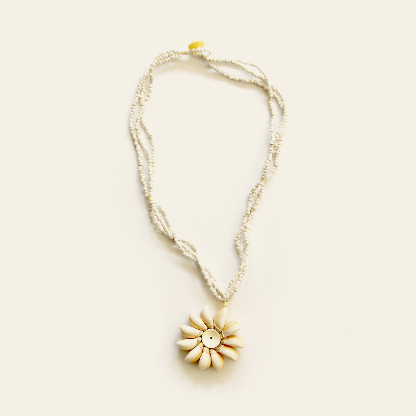 Handmade necklace with white seed bead strands and a central flower pendant made of natural shells arranged in a sunburst pattern — by Nayabijou.