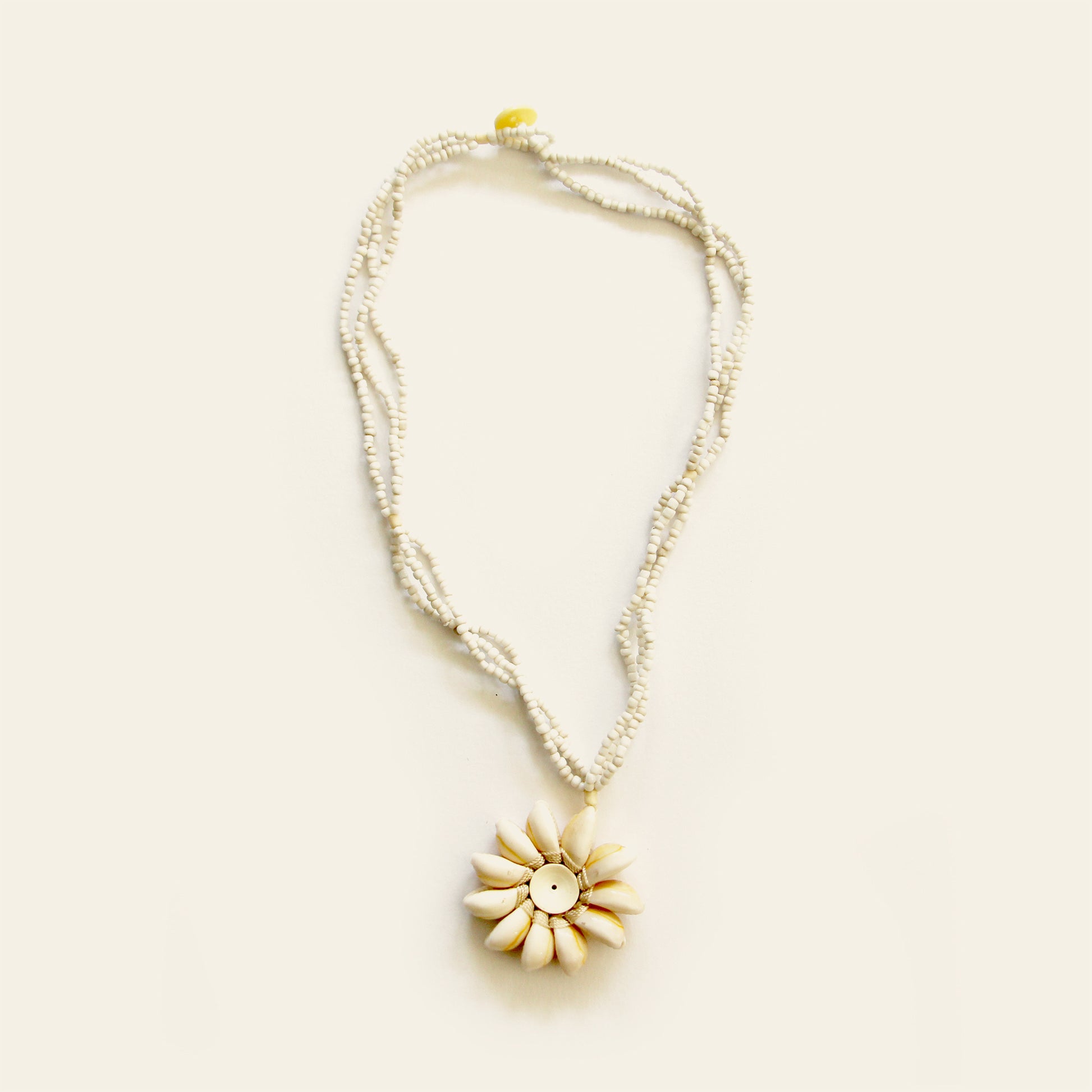 Handmade necklace with white seed bead strands and a central flower pendant made of natural shells arranged in a sunburst pattern — by Nayabijou.