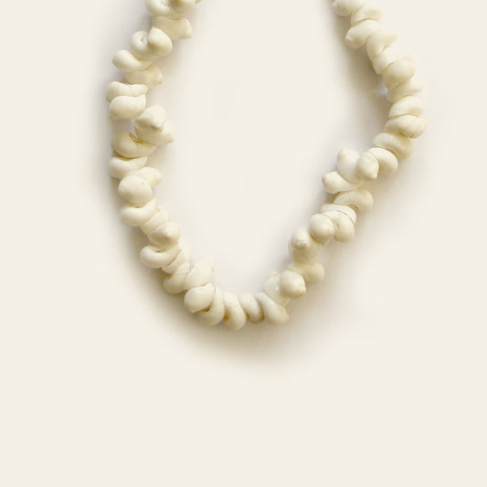 Closeup of handmade bracelet made of white twisted shell beads strung tightly in a natural loop — by Nayabijou.