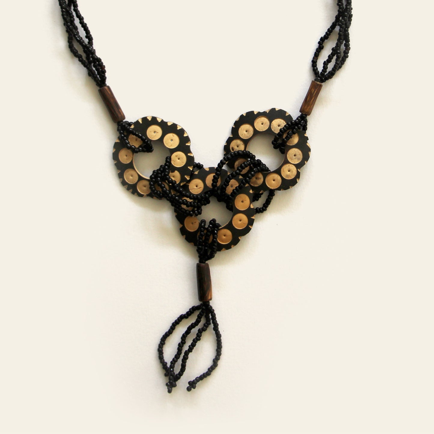 Closeup of a Handmade necklace featuring black seed beads and carved coconut shell loops linked together with beaded knots, finished with a tasseled drop — by Nayabijou.