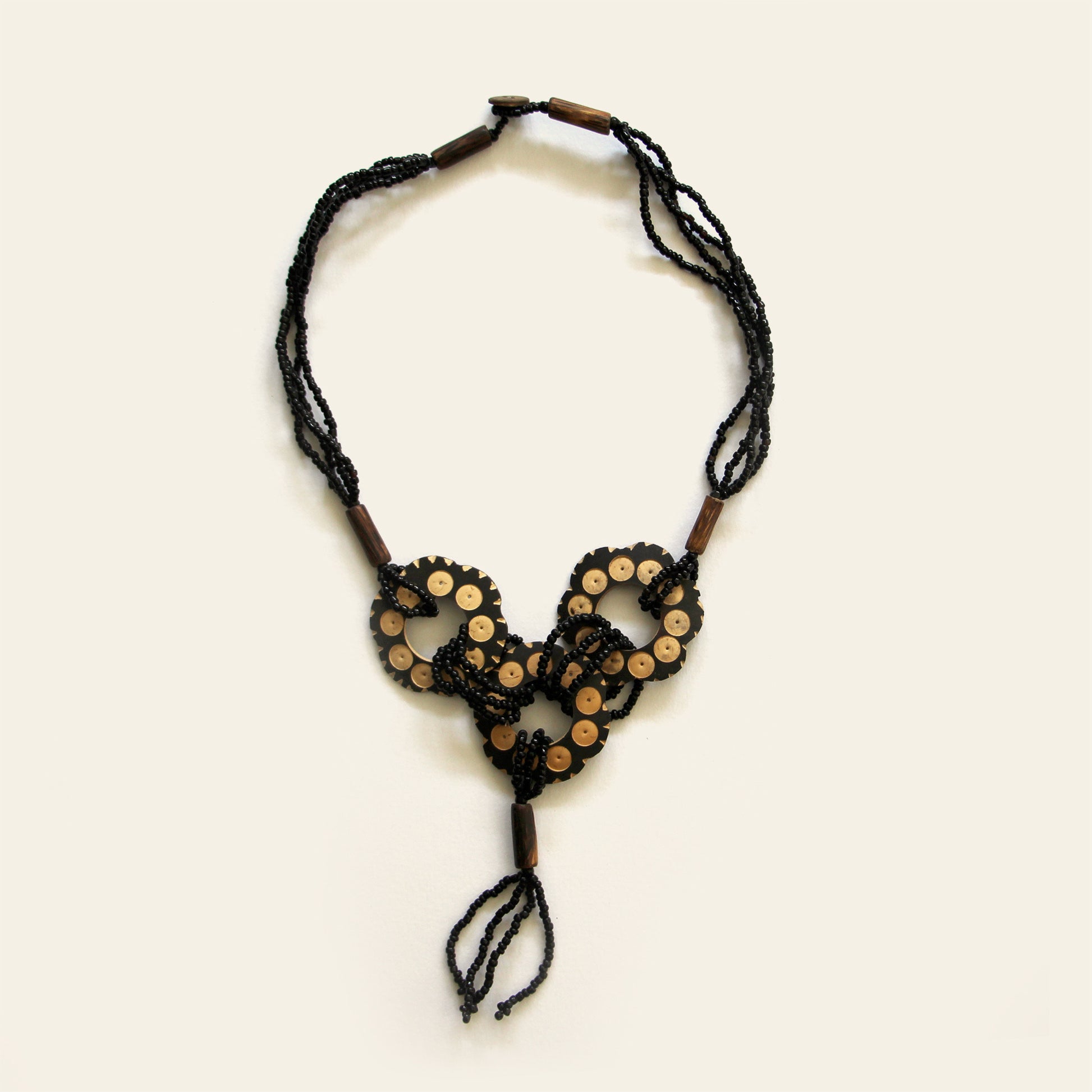 Handmade necklace featuring black seed beads and carved coconut shell loops linked together with beaded knots, finished with a tasseled drop — by Nayabijou.
