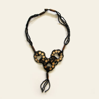Handmade necklace featuring black seed beads and carved coconut shell loops linked together with beaded knots, finished with a tasseled drop — by Nayabijou.