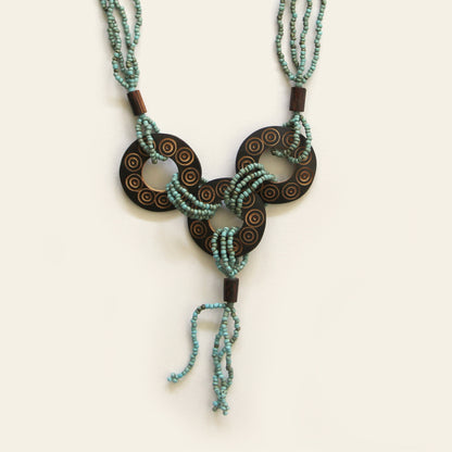 Closeup of a handmade necklace featuring Sand seed beads and carved coconut shell loops linked together with beaded knots, finished with a tasseled drop — by Nayabijou.
