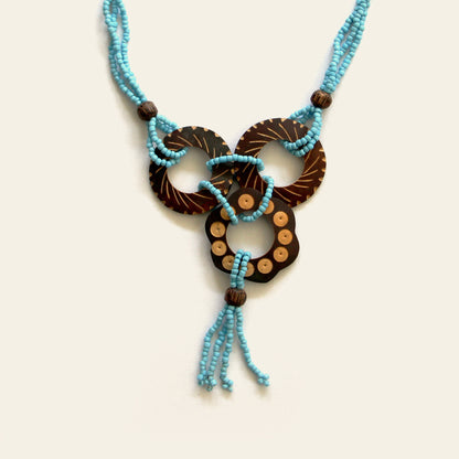 Closeup of a handmade necklace featuring Turquoise seed beads and carved coconut shell loops linked together with beaded knots, finished with a tasseled drop — by Nayabijou.